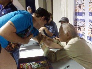 Stan Lee Signing a Man's arm at a comic convention.